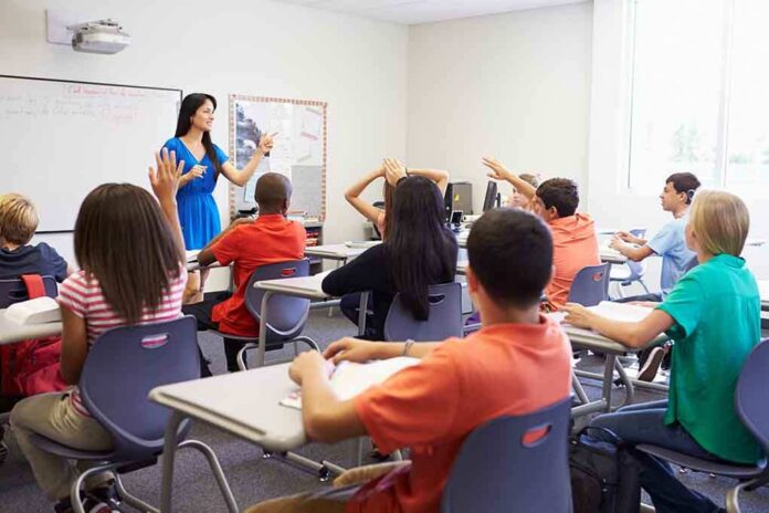 Teacher in a blue dress instructing students in a classroom with hands raised