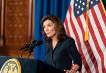 Woman at podium speaking with microphones and U.S. flag behind