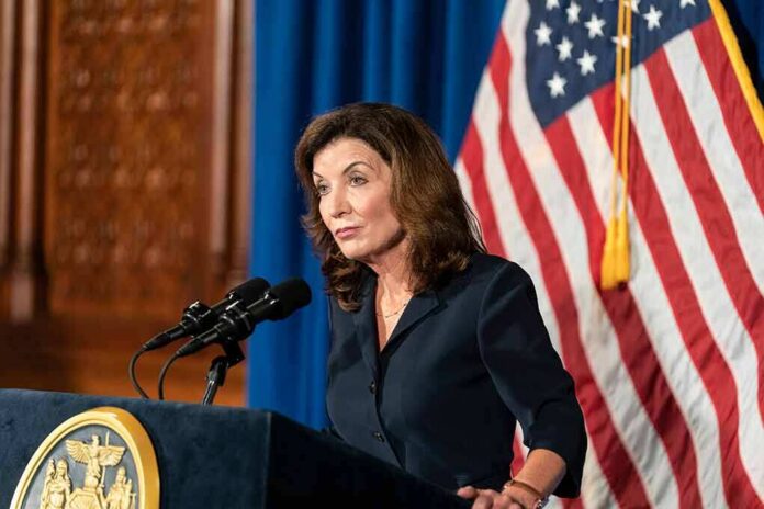 Woman at podium speaking with microphones and U.S. flag behind