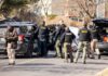 Police and sheriff officers gather around vehicles on a suburban street