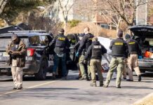 Police and sheriff officers gather around vehicles on a suburban street