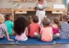 children sitting on mats listening to a teacher read a book