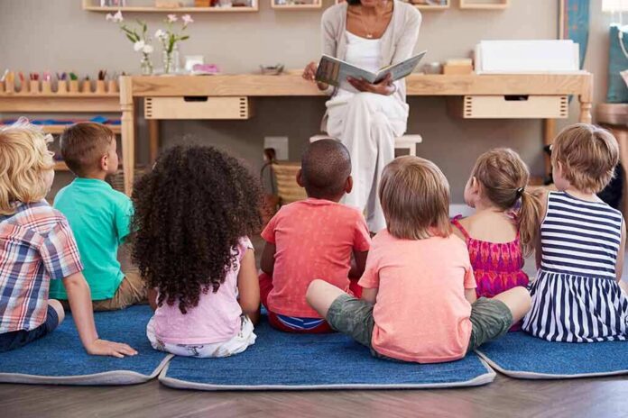 shutterstock_641732326 children sitting on mats listening to a teacher read a book