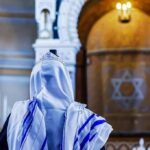 Person in white and blue prayer shawl facing ornate interior