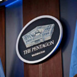 Hegseth Swings Again – Top Ranks Reel The Pentagon emblem between two flags.