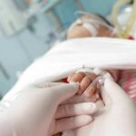 Co‑Sleeping Alibi Crumbles Under Forensics Gloved hands holding a baby's hand in a hospital bed