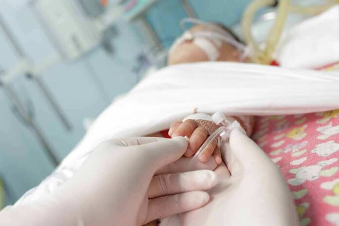 shutterstock_114519565 Gloved hands holding a baby's hand in a hospital bed