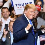 Trump Is Unleashing His Midterm War Chest man in suit raising fists at a rally podium