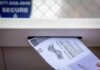 Mail-in ballot being inserted into a secure drop box slot