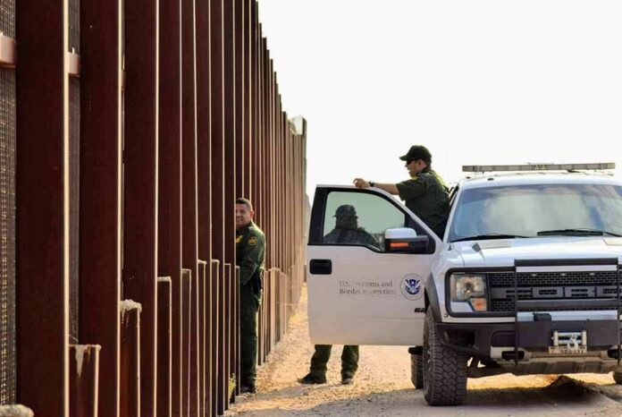 shutterstock_1545833798 Border patrol agents near a tall fence and a marked pickup truck