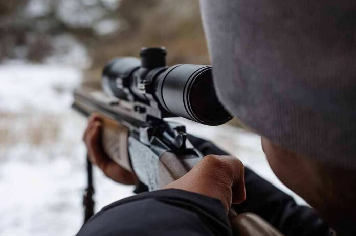 person aiming a rifle with a scope outdoors