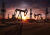 Oil pumpjacks and derricks at sunset in a desert field