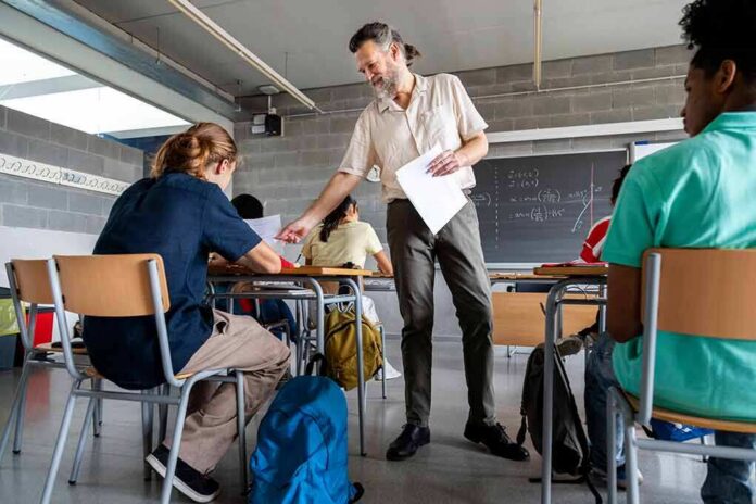 shutterstock_2029939352 Teacher handing out papers in a classroom