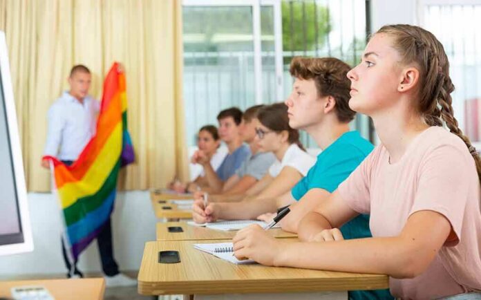 shutterstock_2146129327 Students in a classroom listening as a teacher holds a rainbow flag