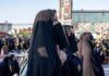 Women in black veils standing among a crowd outdoors