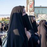 Women in black veils standing among a crowd outdoors