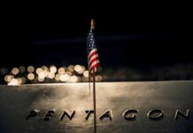 Pentagon Shock: 9/11 Message Hits Hard Small American flag on a memorial with bokeh lights at night