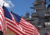 American flags in front of a naval ship under a blue sky