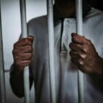 Person gripping prison bars with both hands