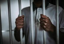 Celebrity Pardon Play Backfires – Guess Who Person gripping prison bars with both hands