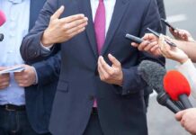 Businessperson in suit speaking to reporters with microphones