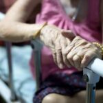 Elderly person’s hands resting on a hospital bed rail