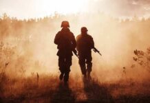 Two soldiers walking through a smoky field at sunset