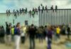 People sitting atop a tall border fence during a protest