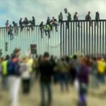 Open-Borders Push Or Chaos Gambit? People sitting atop a tall border fence during a protest