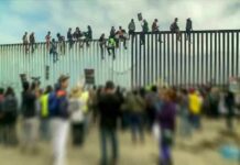 People sitting atop a tall border fence during a protest