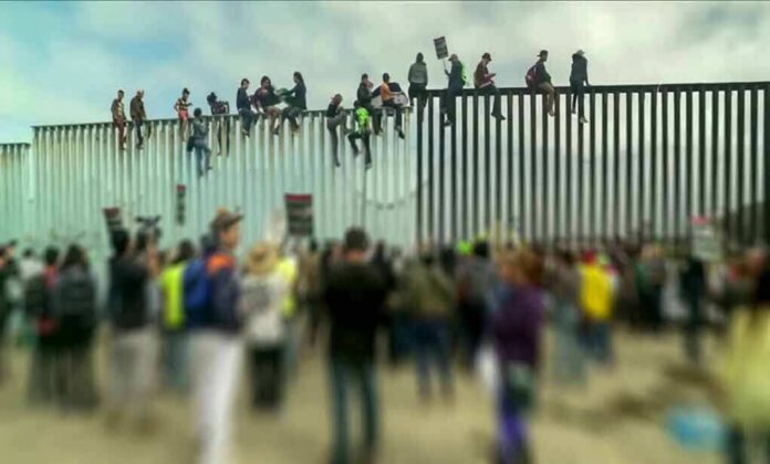 People sitting atop a tall border fence during a protest