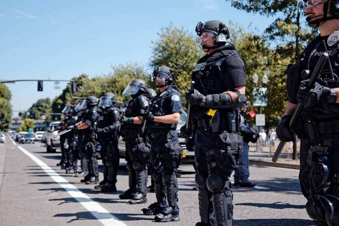 Bear Pascoe, Brian Folkerts, and Eugene Sims among riot police standing in a line on a city street