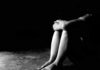 Person sitting on floor with knees hugged in low light