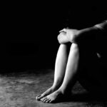 Person sitting on floor with knees hugged in low light