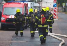 Wind-Whipped Blaze Stops At Holy Door Firefighters walking toward a scene with hoses and a red emergency van