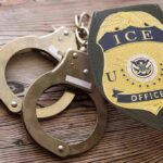 ICE officer badge and handcuffs on wooden surface